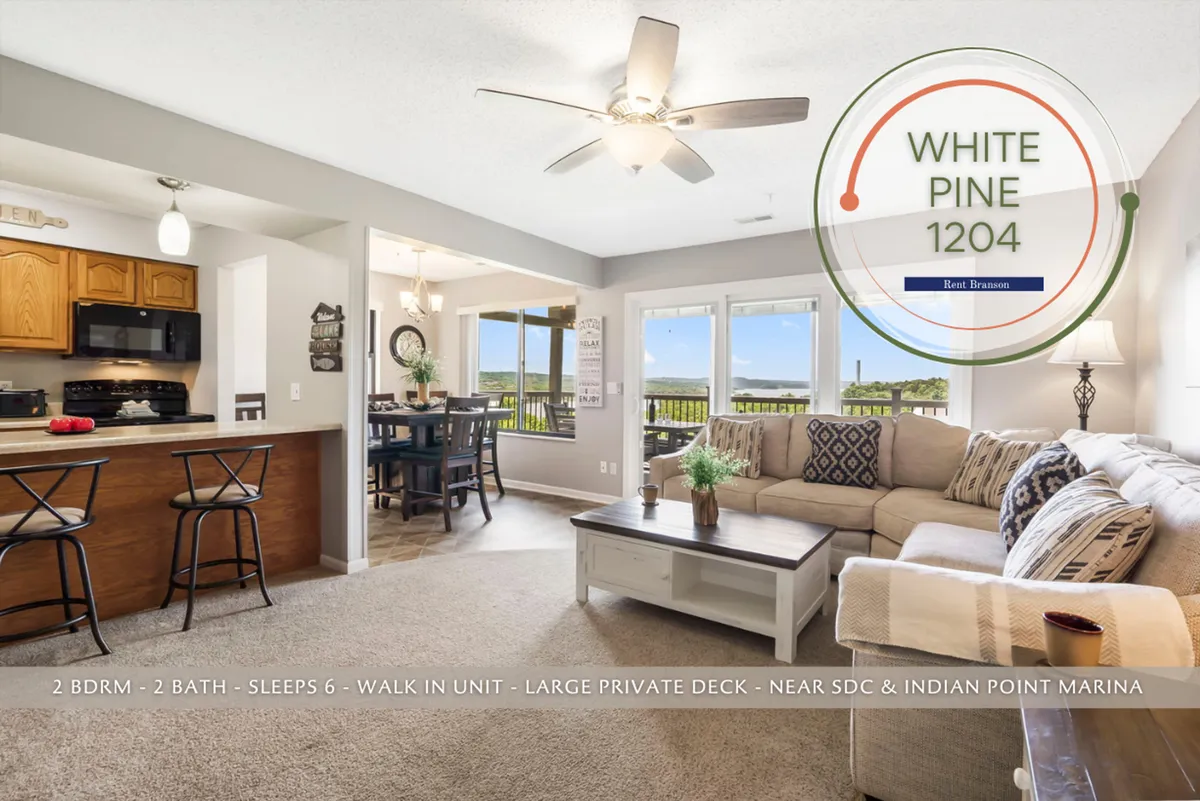 This image features a comfortable sectional sofa set in a spacious open-concept living area, with large windows letting in abundant natural light. The view through the windows showcases the scenic outdoors, and the dining area and kitchen island are visible, emphasizing the communal aspect of the space.