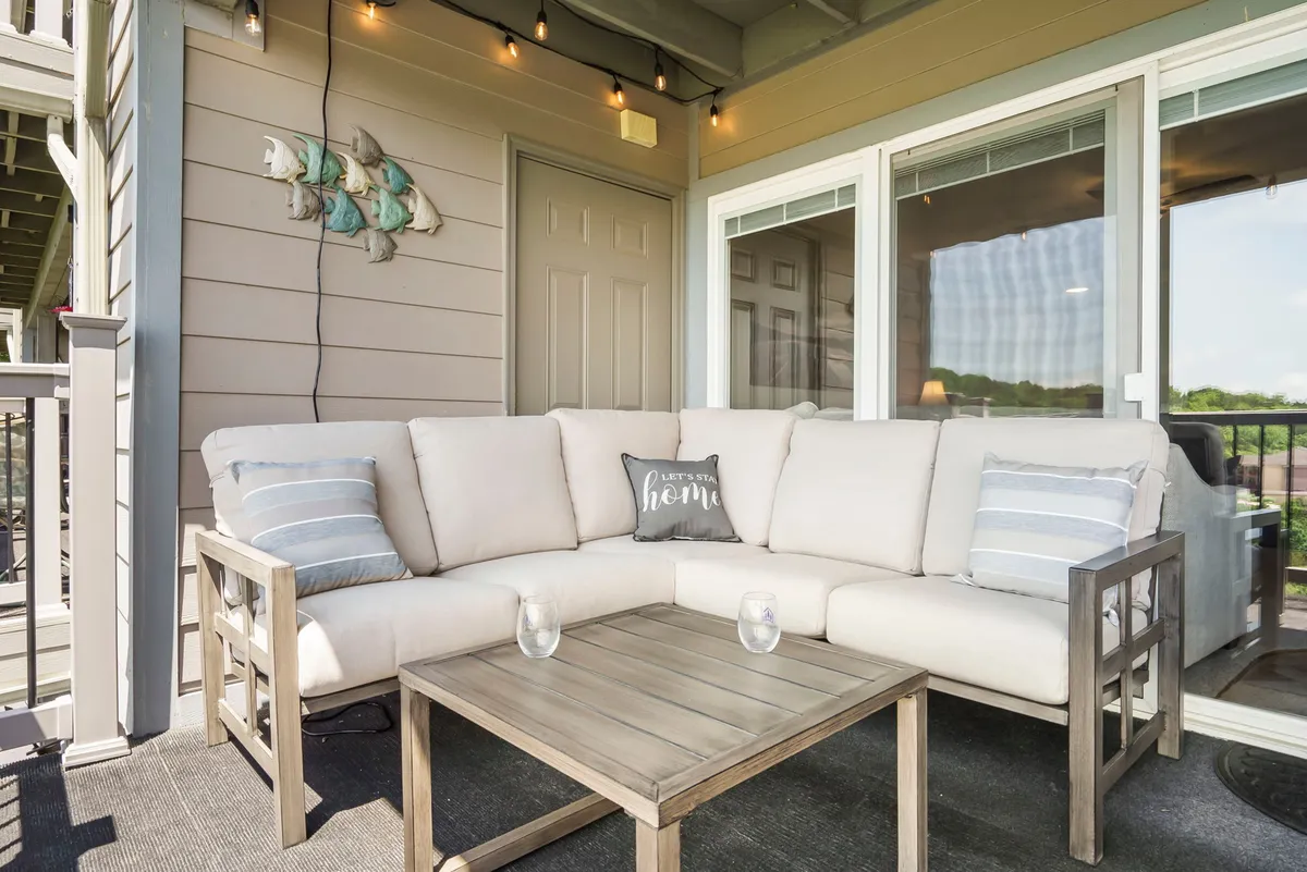 A spacious private deck featuring a comfortable sectional sofa with decorative pillows, a wooden coffee table, and string lights overhead. The setting overlooks a scenic outdoor view, creating a perfect space for relaxation or entertaining guests.