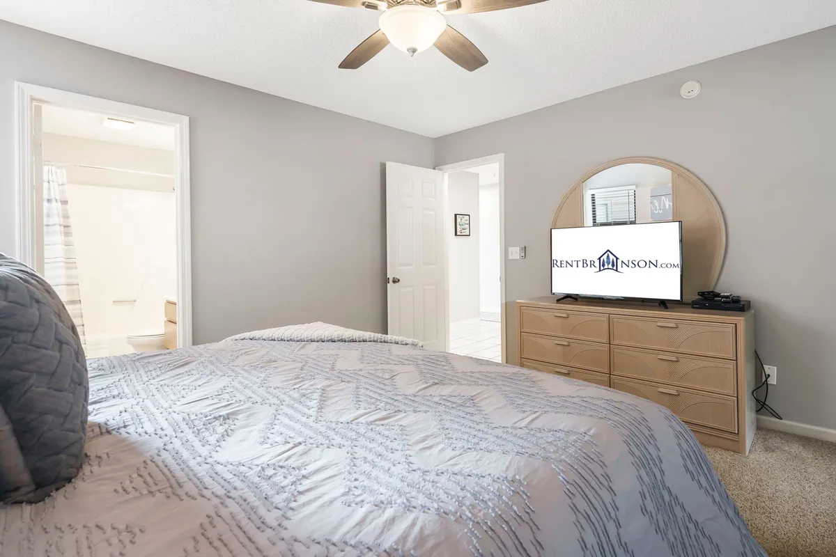 A cozy bedroom featuring a bed with textured bedding, a round mirror above the dresser, and a TV perfectly positioned for in-bed viewing. The space is bright, welcoming, and designed for relaxation, with subtle décor accentuating comfort and tranquility.