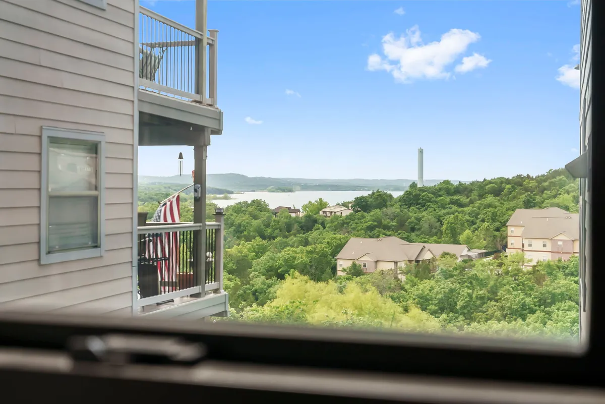 A breathtaking view of the lake framed by lush green landscape and distant hills, as seen from a vantage point that could be the condo's balcony or living area. The tranquil scene sets the tone for peaceful downtime after busy days at local attractions.