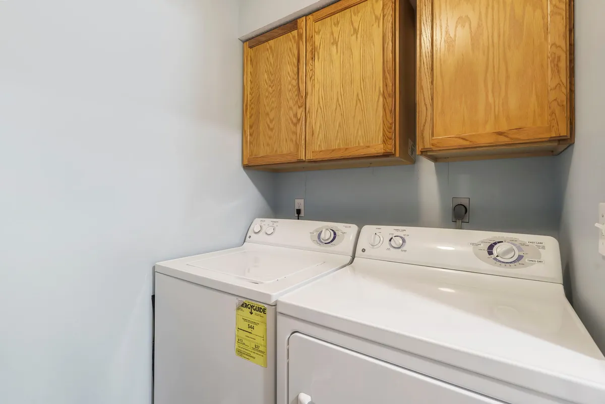 A bright, tidy laundry room featuring a washing machine, dryer, and wooden cabinetry, suggesting daily convenience and practicality within the condo.