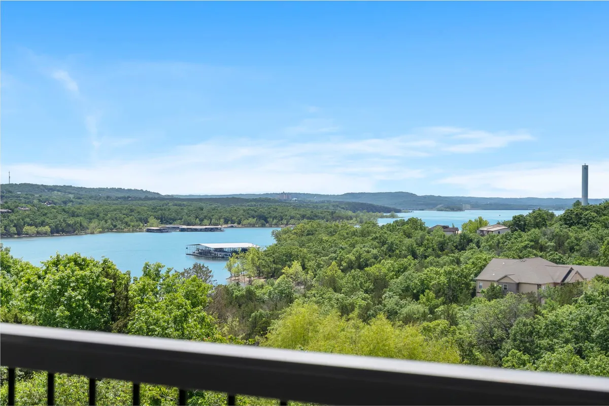 The image showcases a breathtaking view of the lake framed by lush green trees, with distant rolling hills beneath a clear blue sky. The tranquil scene evokes the natural beauty and serenity surrounding the condo, hinting at opportunities for boating, hiking, and relaxing in nature.