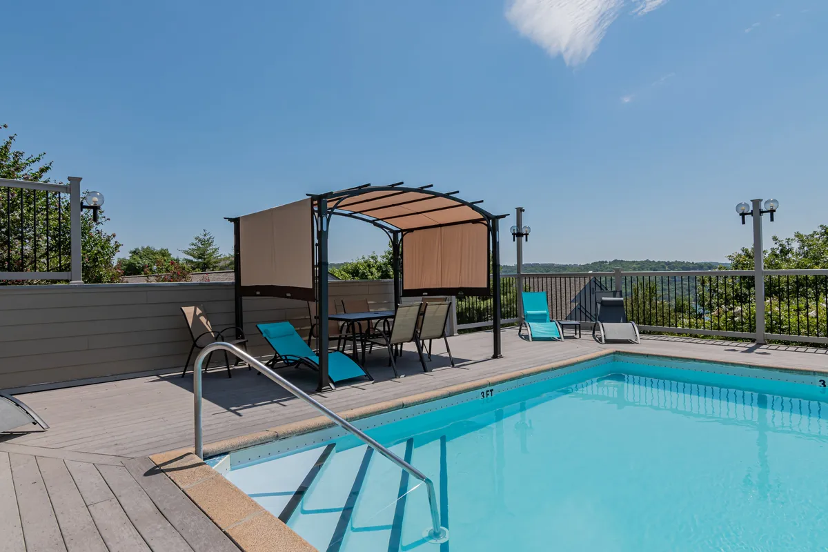 This image shows a sparkling outdoor swimming pool surrounded by lounge chairs and a canopy, with a scenic landscape visible in the background. The inviting setup suggests a place to relax, swim, and gather as a family during the warmer months.