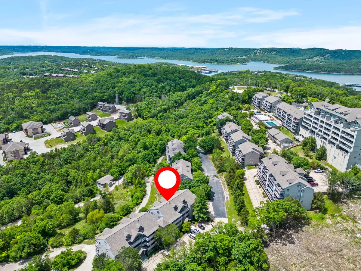 A serene exterior shot featuring lush green trees, a clear waterfront view, and the modern architecture of nearby buildings. Winding paths suggest opportunities for hiking and outdoor exploration.