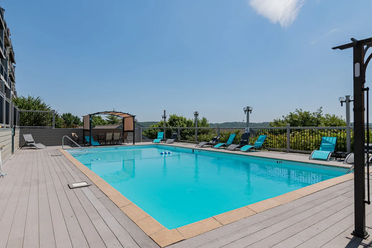 An inviting exterior scene of a sparkling outdoor swimming pool surrounded by lounge chairs, a canopy structure, and a landscape view that hints at the resort's overall amenities. The pool area is serene, suggesting seasonal enjoyment for guests of all ages.