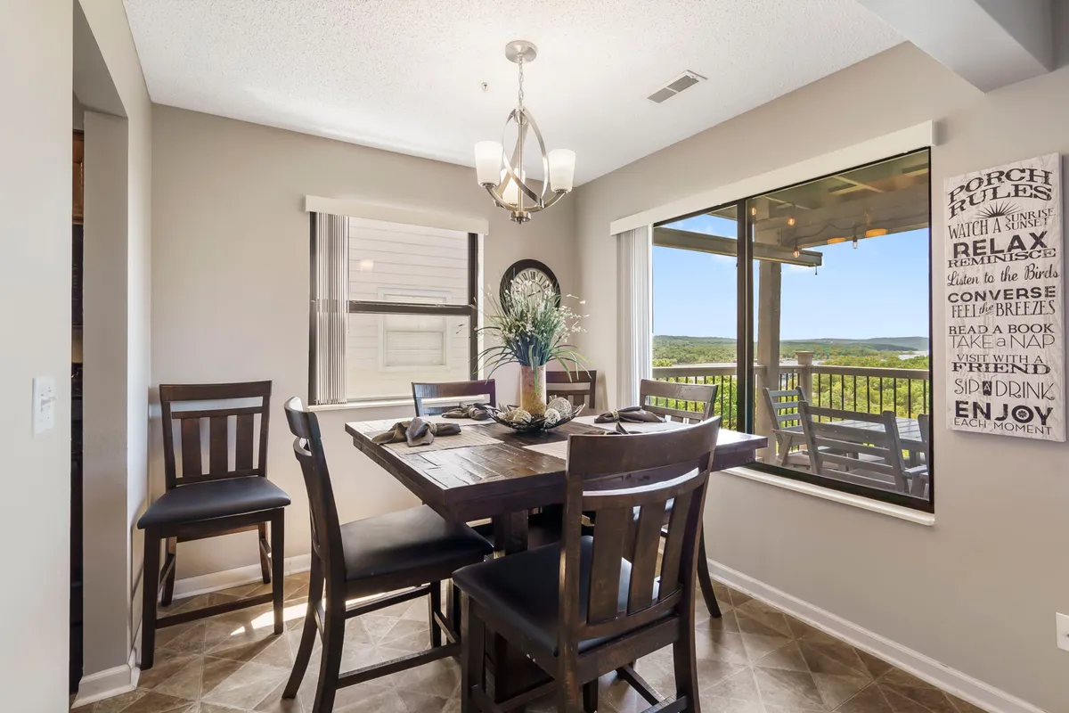 A well-lit dining area is shown with a family-sized table, stylish decor, and expansive windows offering a scenic view outside. The atmosphere is warm and inviting, suitable for meals, games, or socializing.