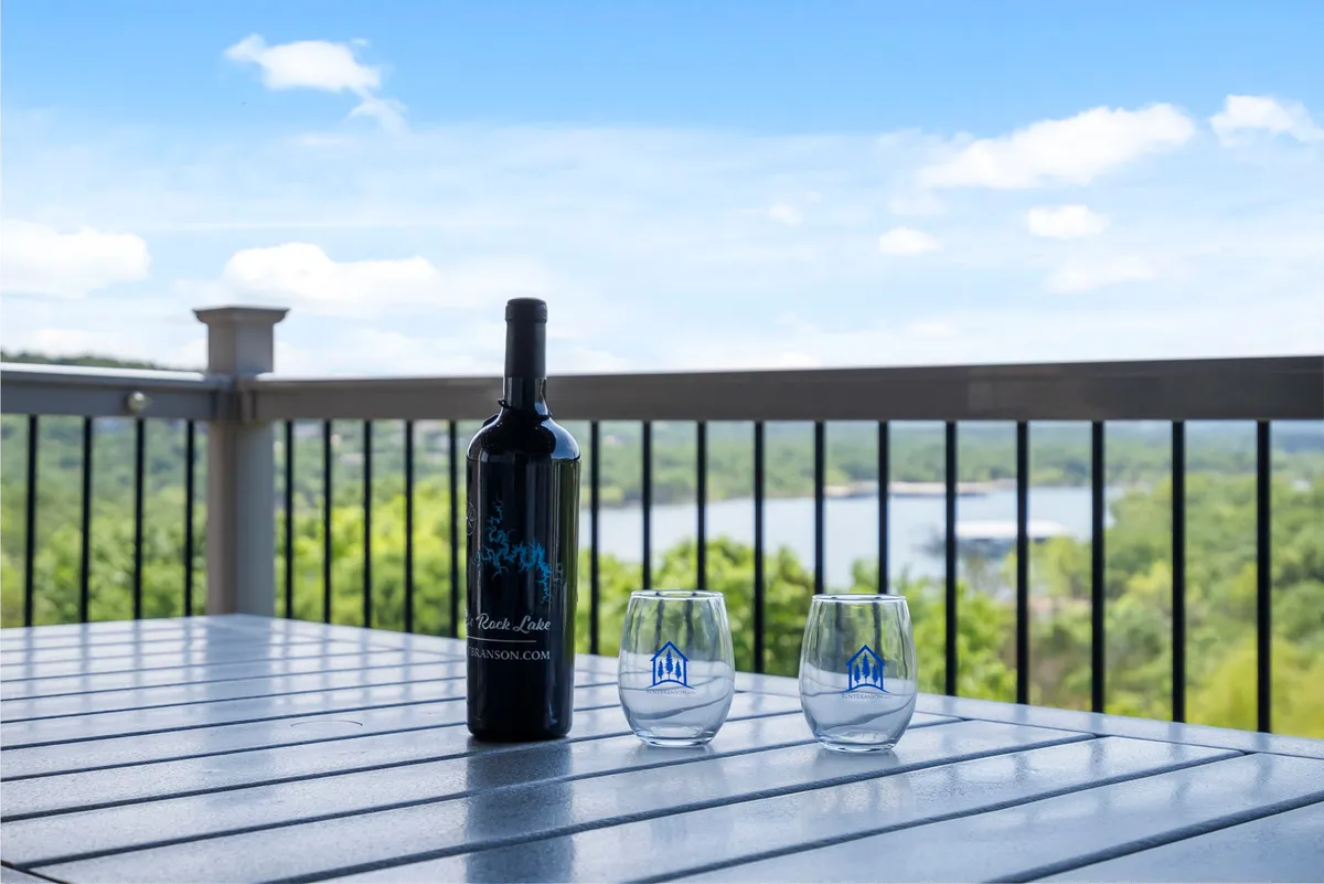 An exterior shot of a private balcony, featuring a wine bottle and two glasses set on a small table, with a sweeping scenic view of the lake and surrounding nature in the background. The space radiates tranquility and is ideal for enjoying morning coffee or evening relaxation while taking in the expansive lake views.